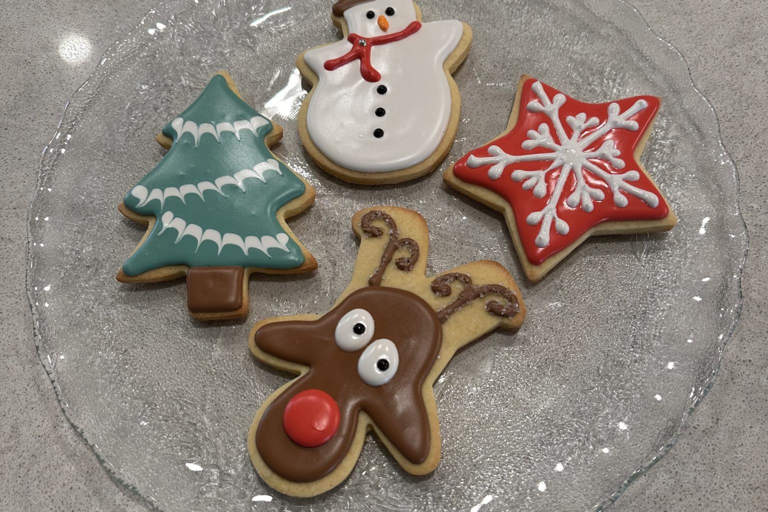 Decorated Christmas cookies on a glass plate: tree, snowman, star, and reindeer.