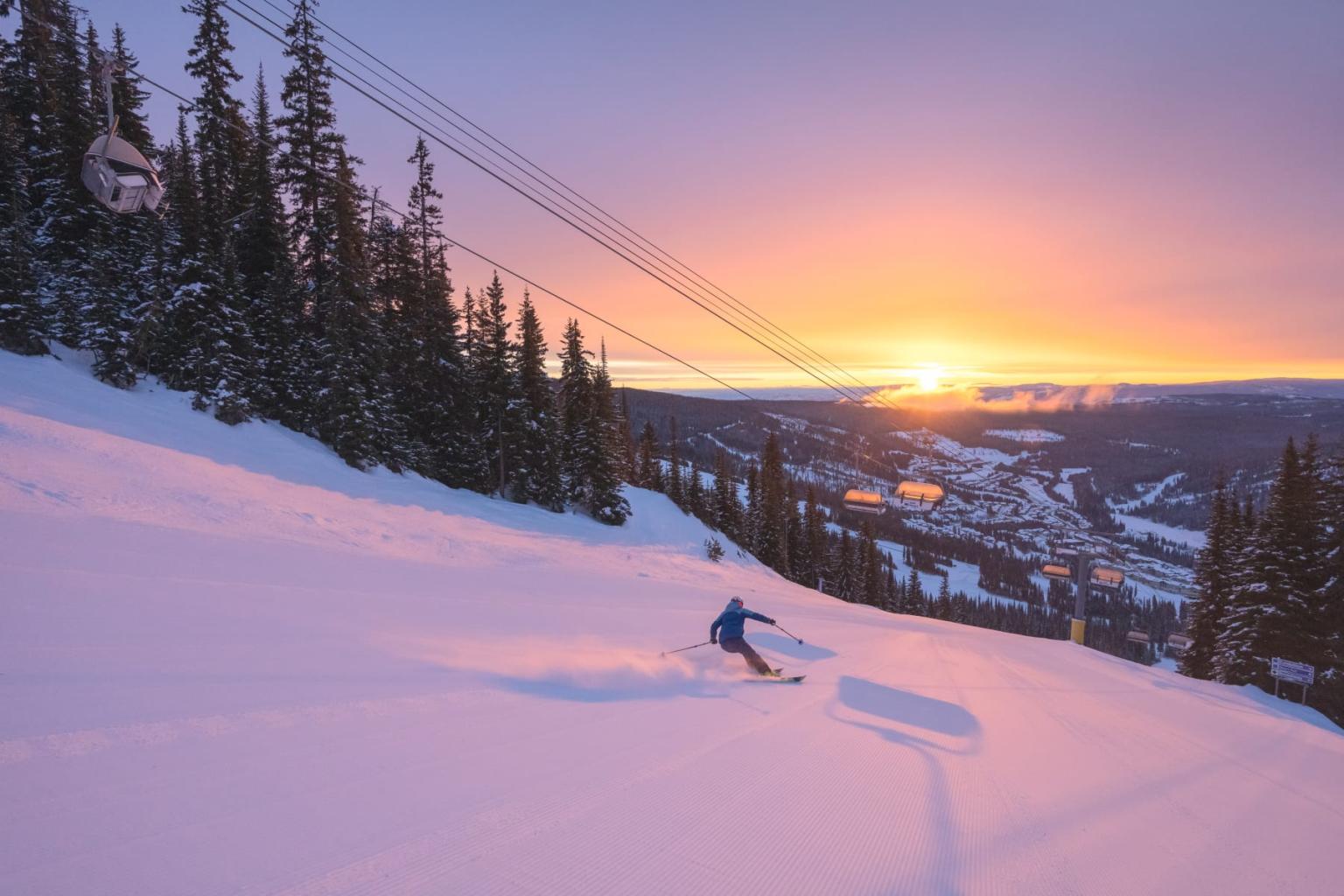 Skier carving through pink sunset snow on a mountain slope.