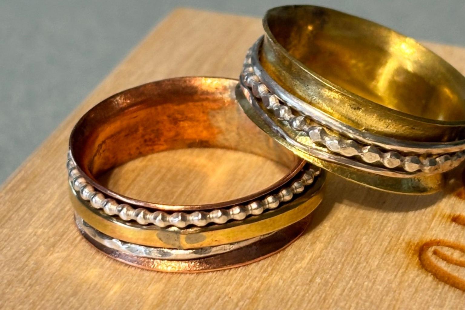 Two gold rings with silver beaded bands on a wooden surface