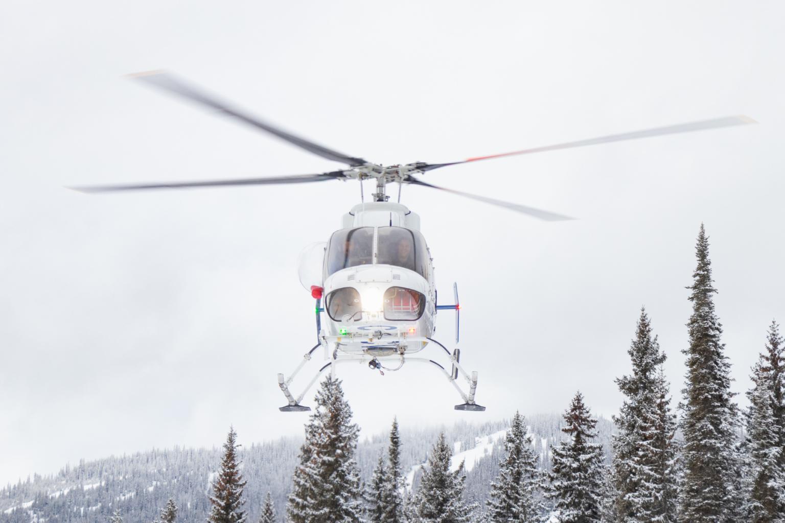 A helicopter flying above trees with a white sky in the background