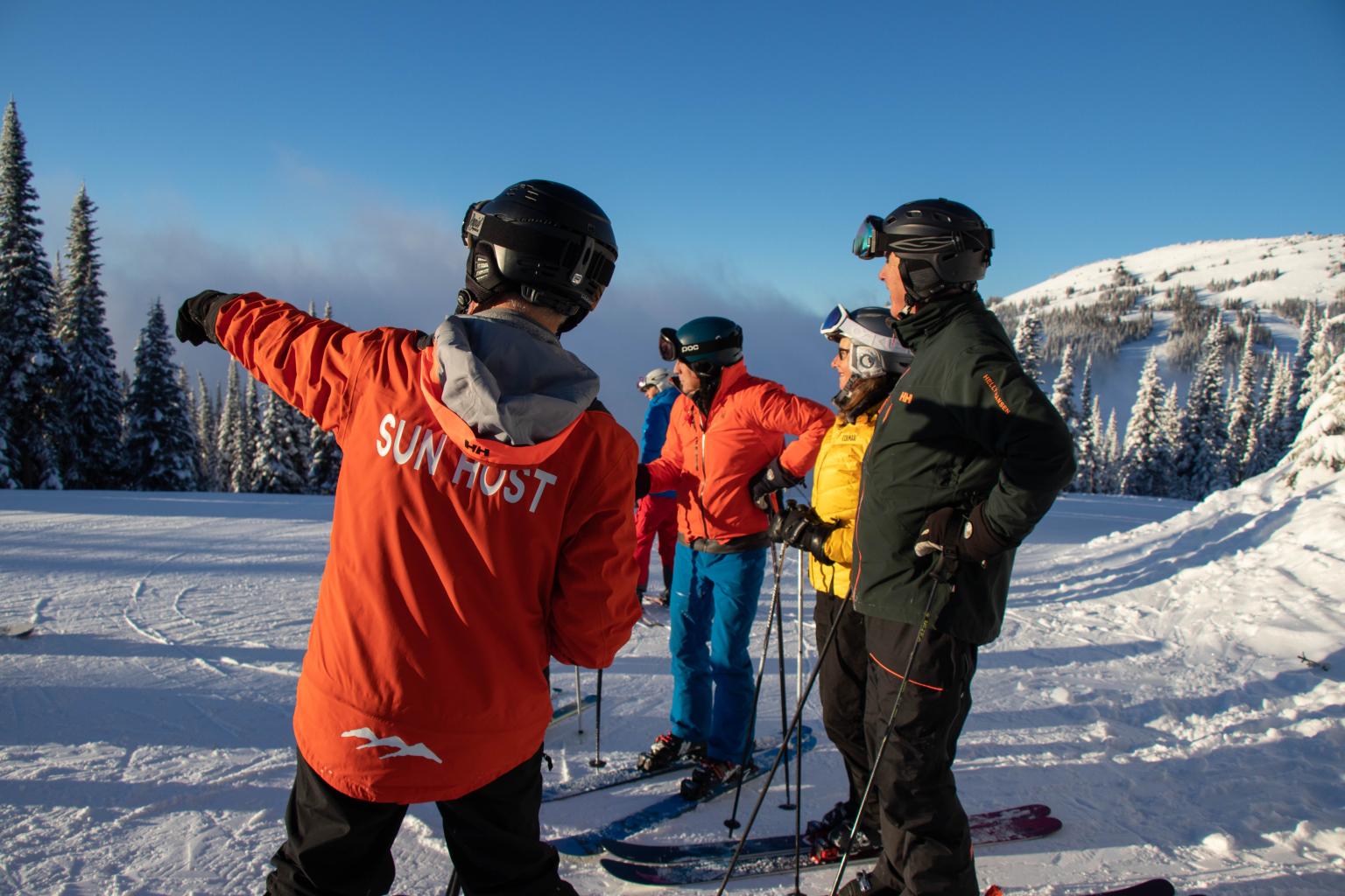 Sun Host pointing to the landscape with fellow skiers