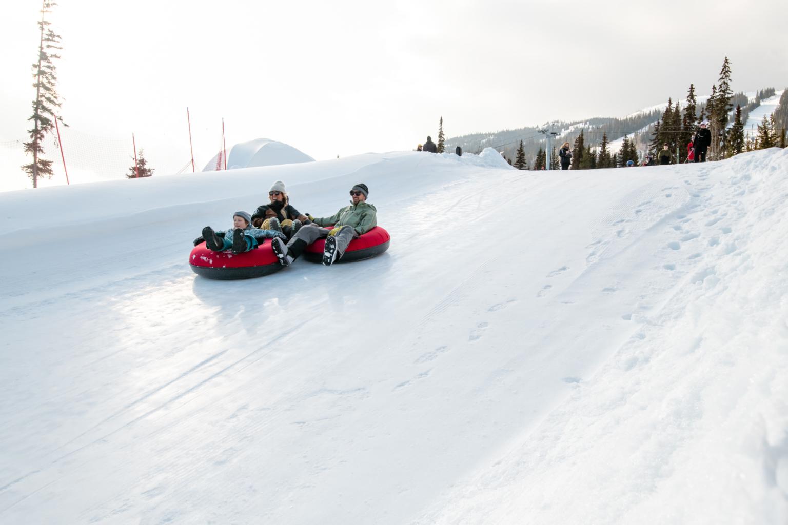 Three people on red tubes tubbing with mountains behind them 
