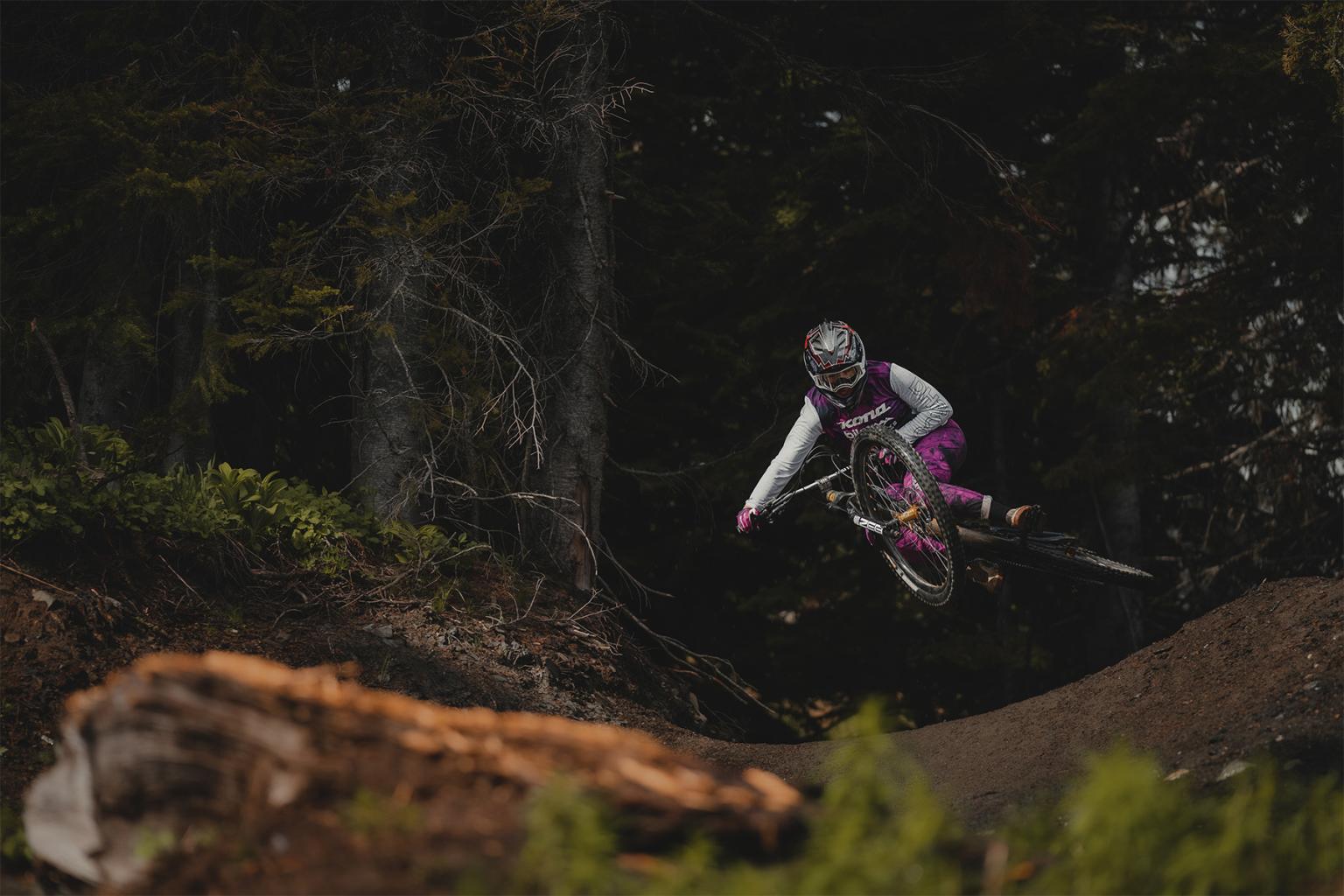 Kyleigh Stewart whipping her mountain bike over a jump in the forest