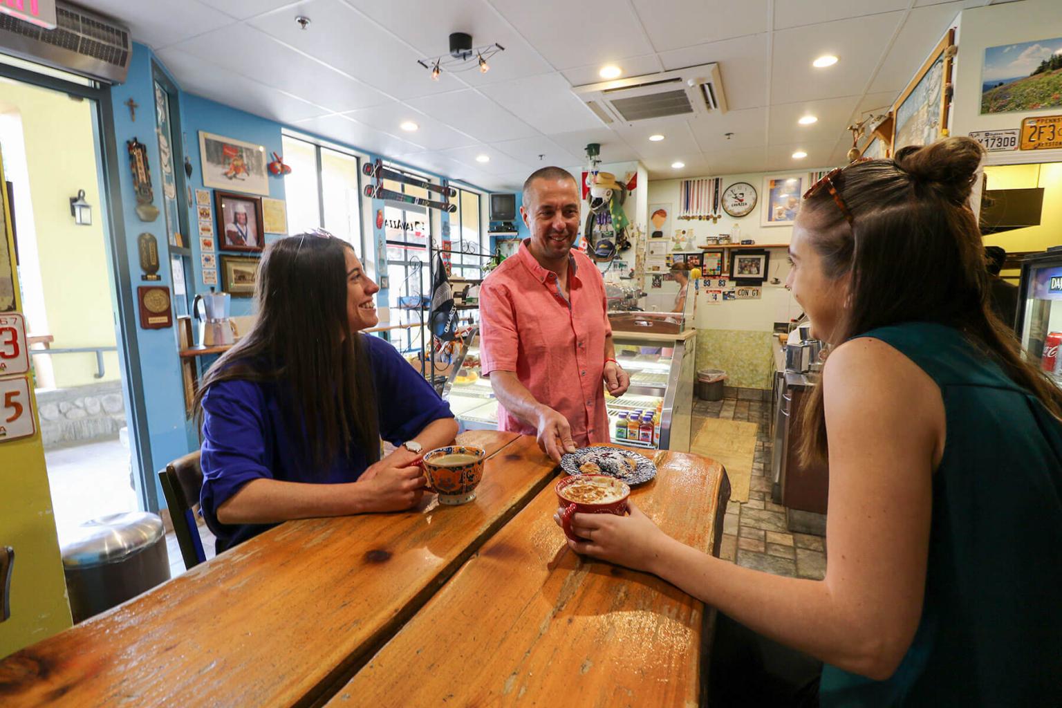 Two people sitting at a table being served coffee inside of a coffee shop