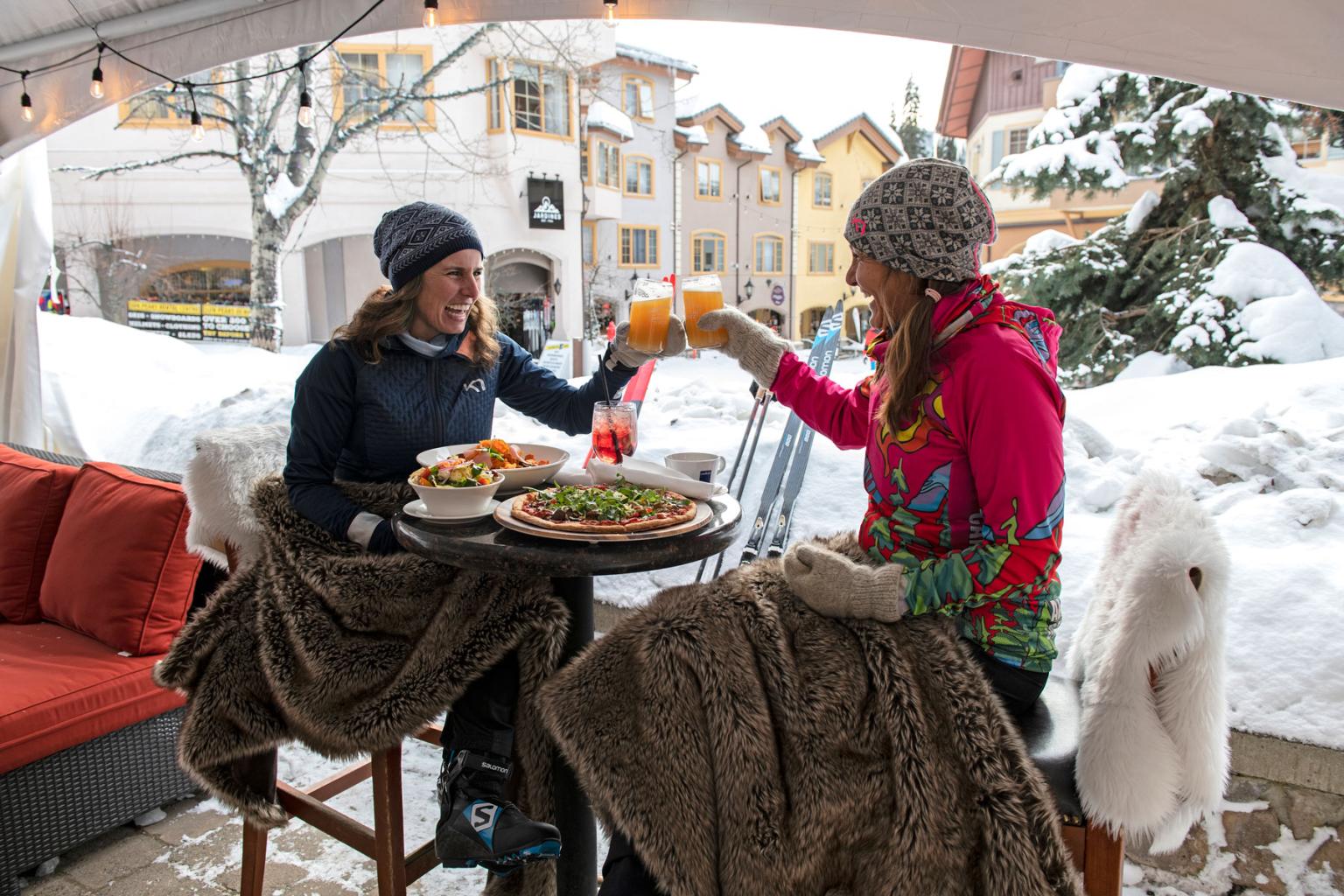 Two people on a patio with drinks and meals clinking their glasses together