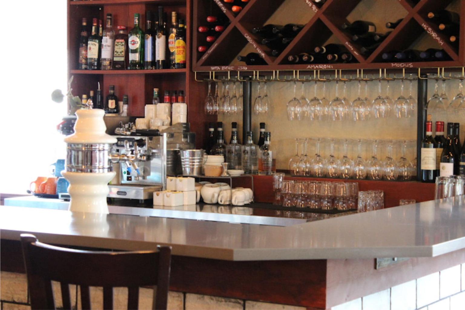 A view of a bar with wine glasses hung up and liquor bottles lined up