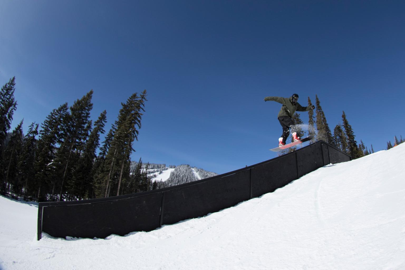 Snowboarder on a rail with mountain views