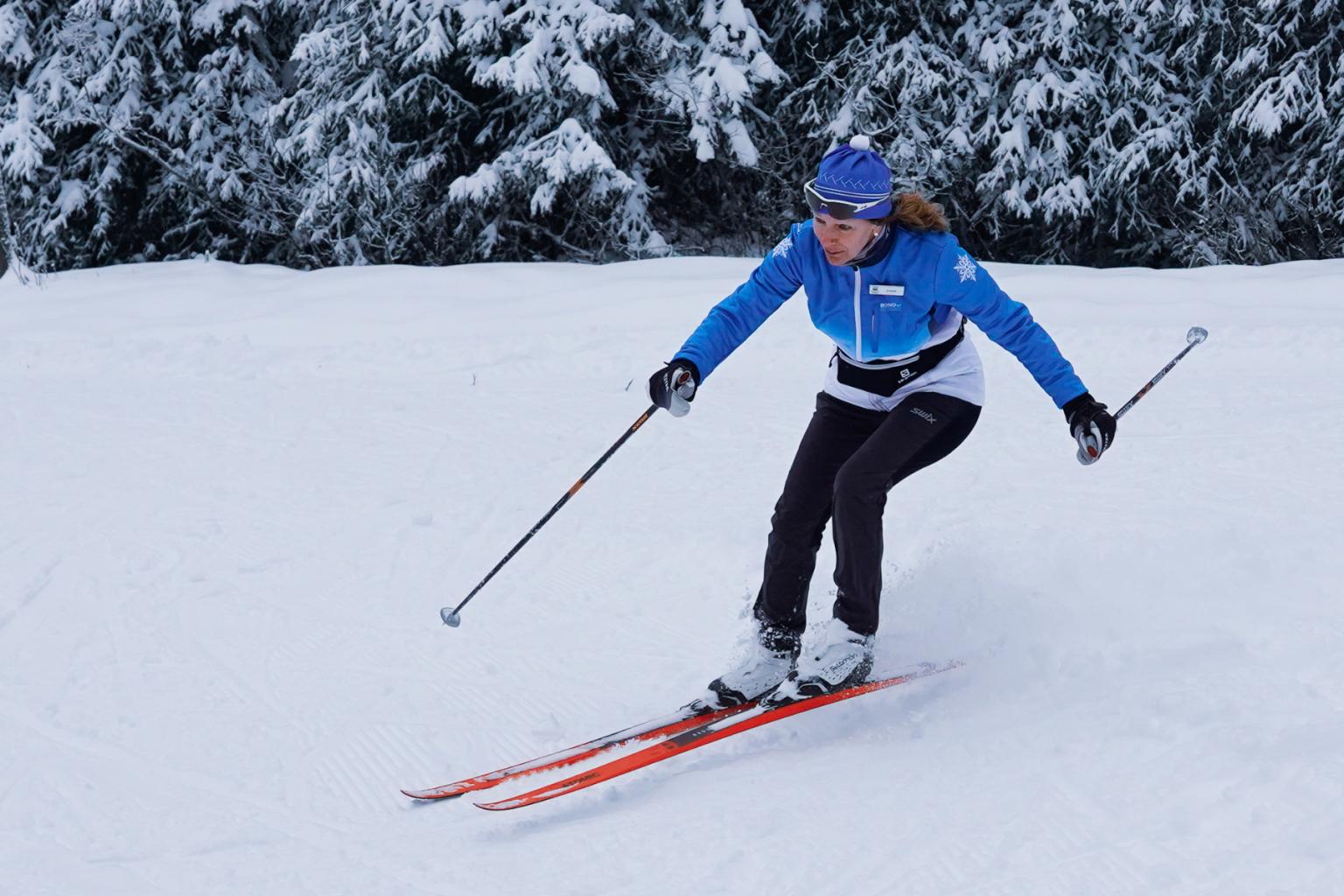 A Nordic skier riding down a hill with snow covered trees around her