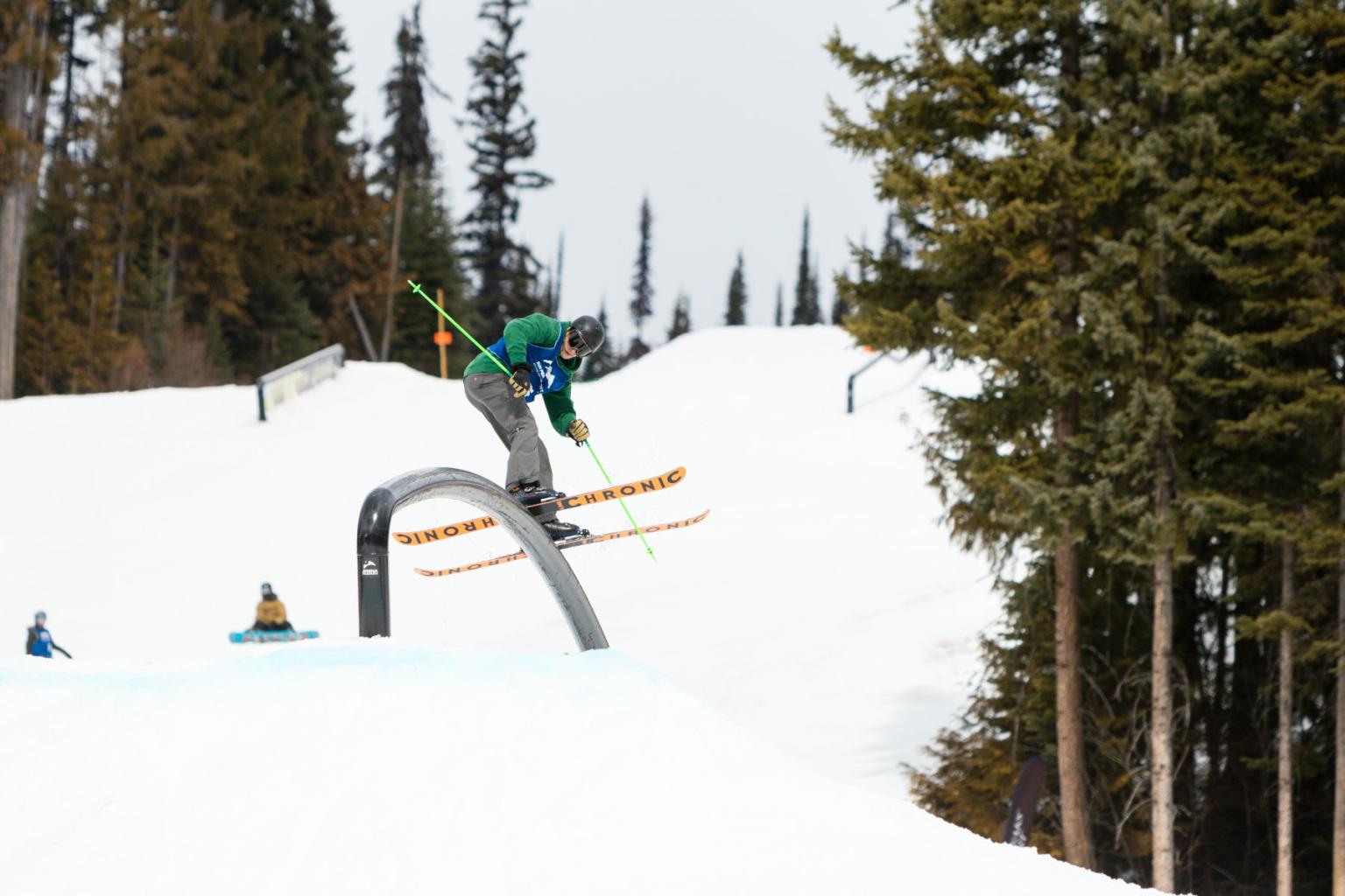 Skier hitting a rail in the terrain park with trees around them