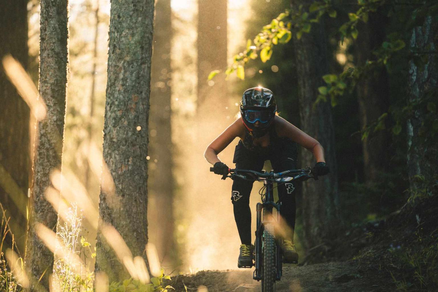 Downhill biker riding down a trail with trees surrounding them
