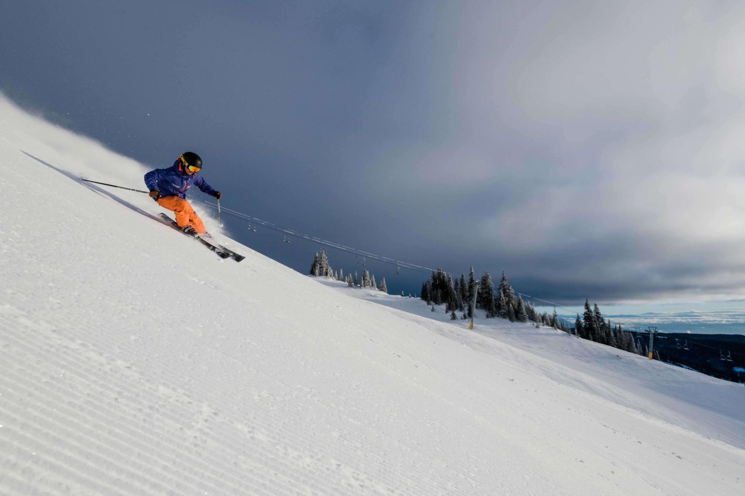 Skier riding down freshly groomed snow with mountain views in the background