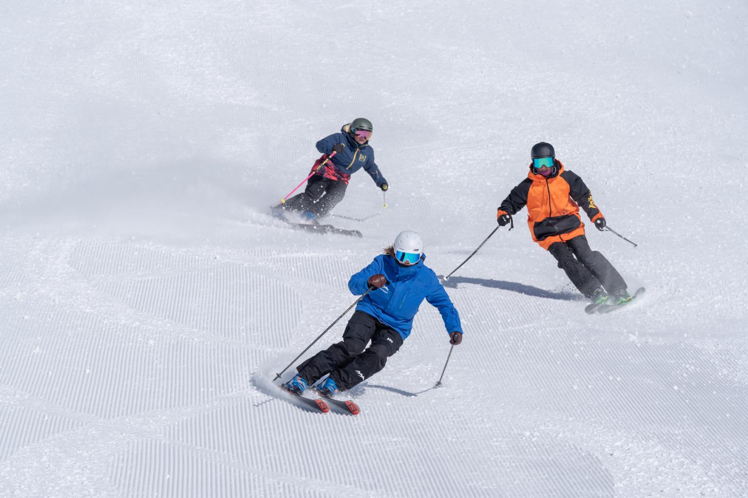 Three skiers skiing down the hill on freshly groomed snow
