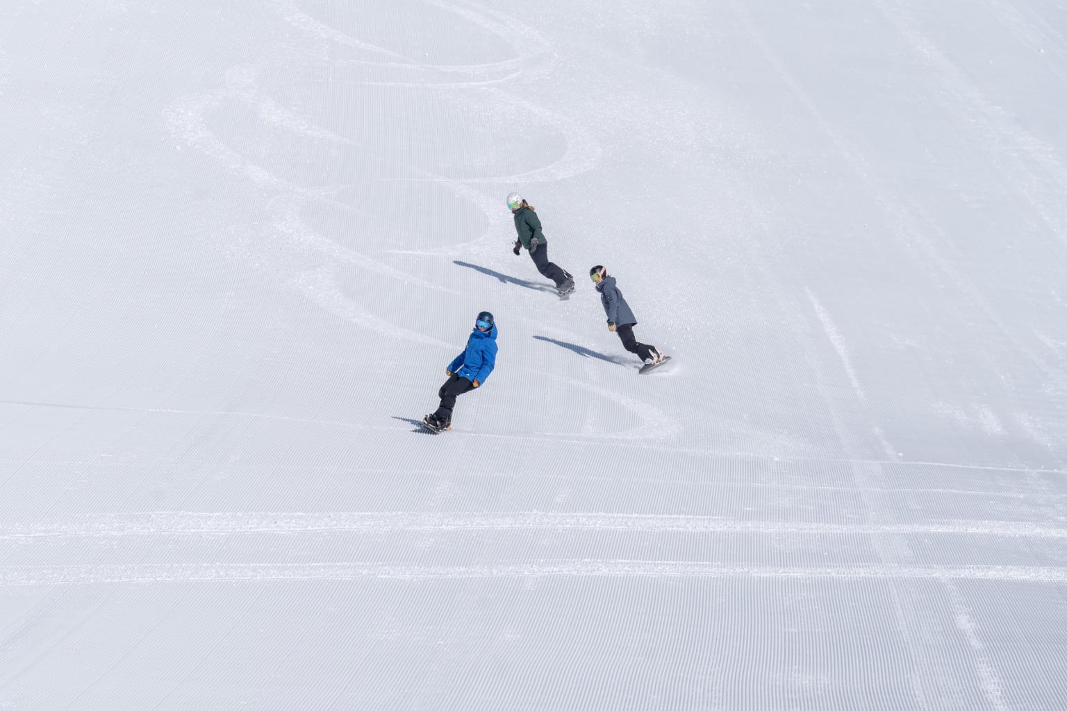 Three snowboarders riding down the hill on freshly groomed snow