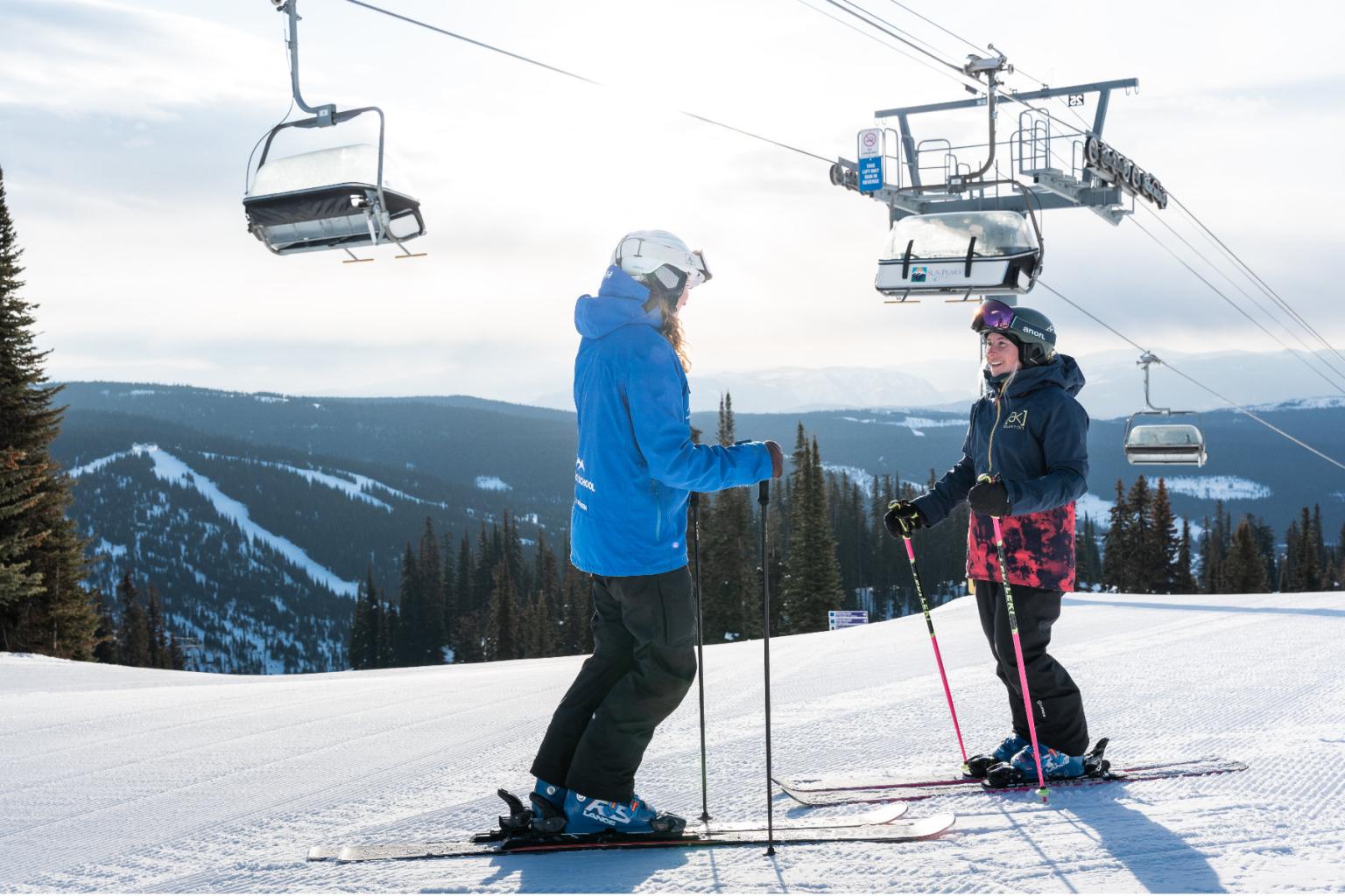 Two skiers facing eachother under the chair lift with mountain views in the distance