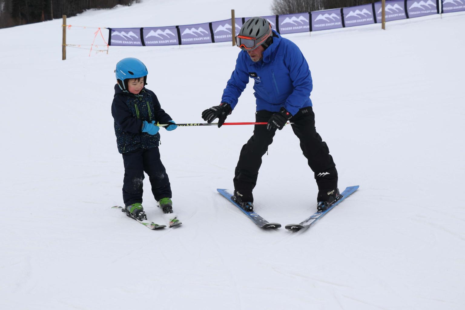 An adult and child on skis holding onto a ski pole 