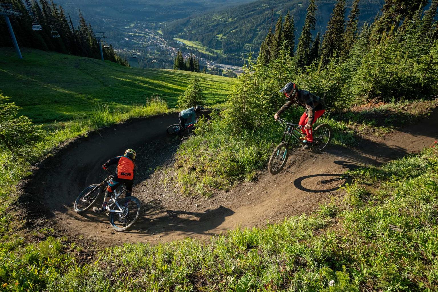 Two bikers going down a trail with lush greens around them and the village in the distance