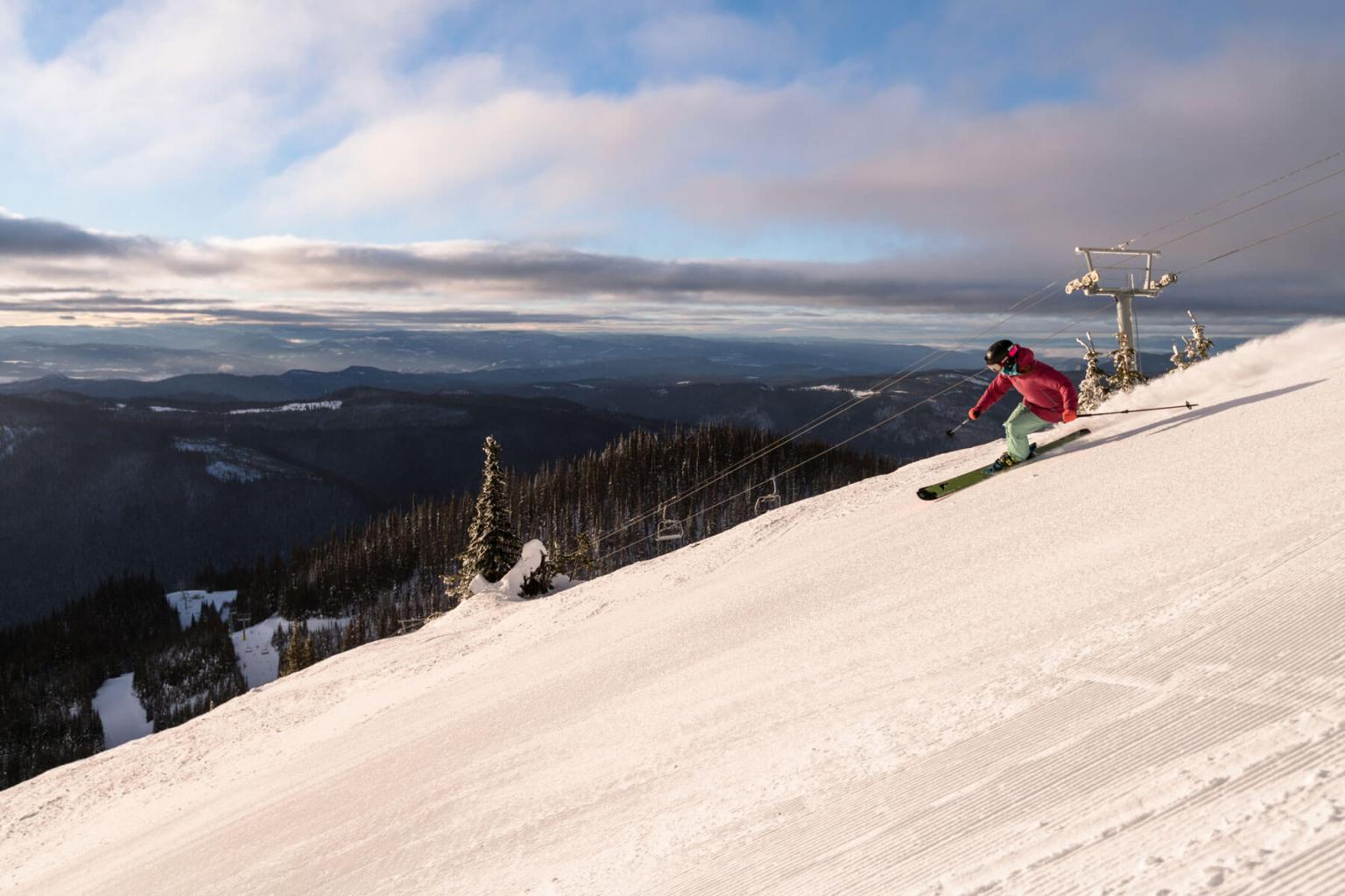 Skier carving on freshly groomed snow with the chairlift and mountains in the background