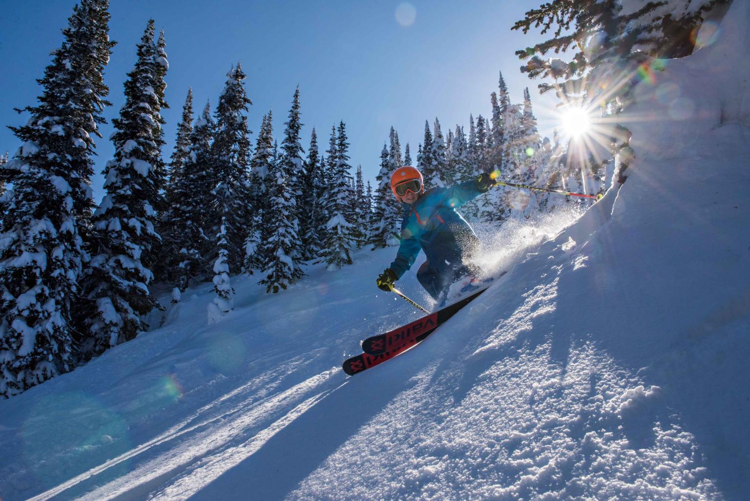 A child skier riding down a run with trees and blue skies in the background