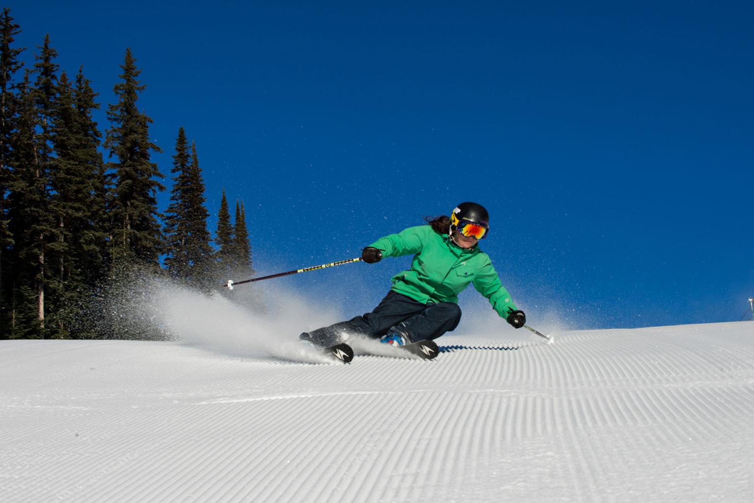 A skier carving down freshly groomed snow with blue skies in the background