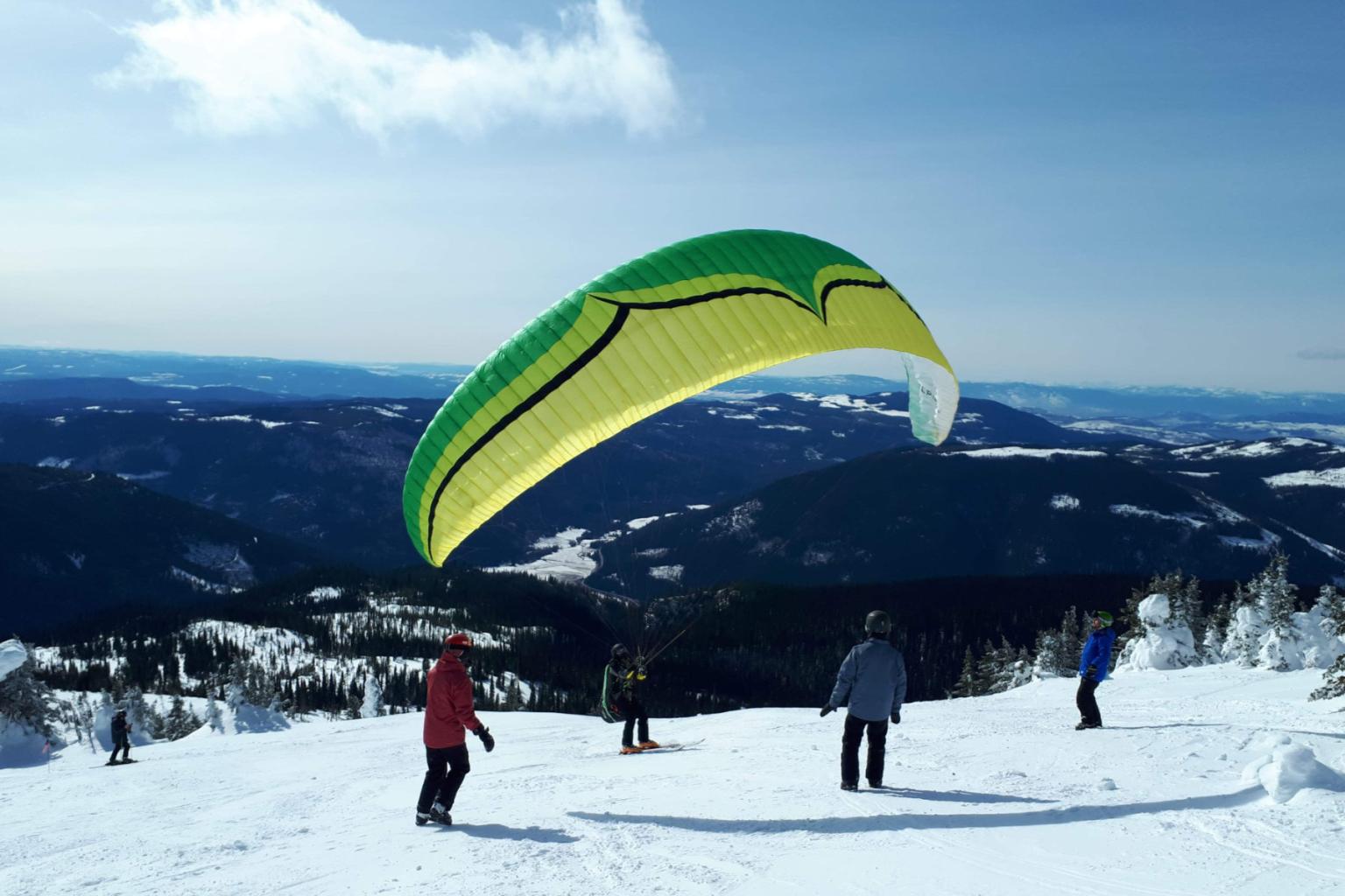 Four people on mountain with a hang glider in the wind with mountain views