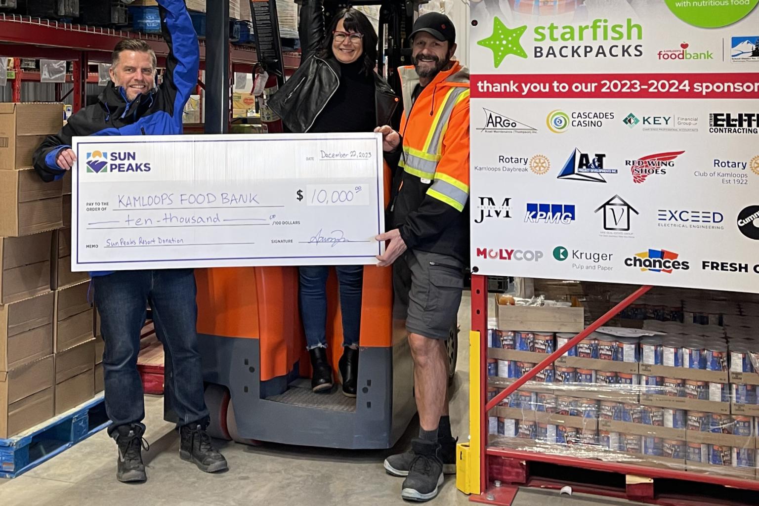 Three people holding a big cheque and smiling in a warehouse