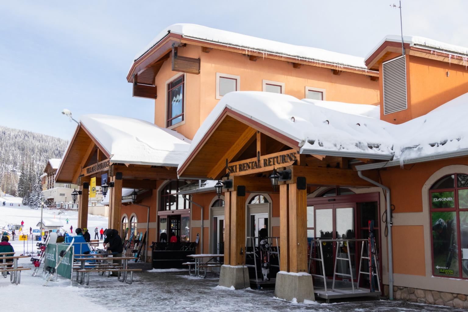 View of the outside of a building with skiers and snowboarders standing outside of it