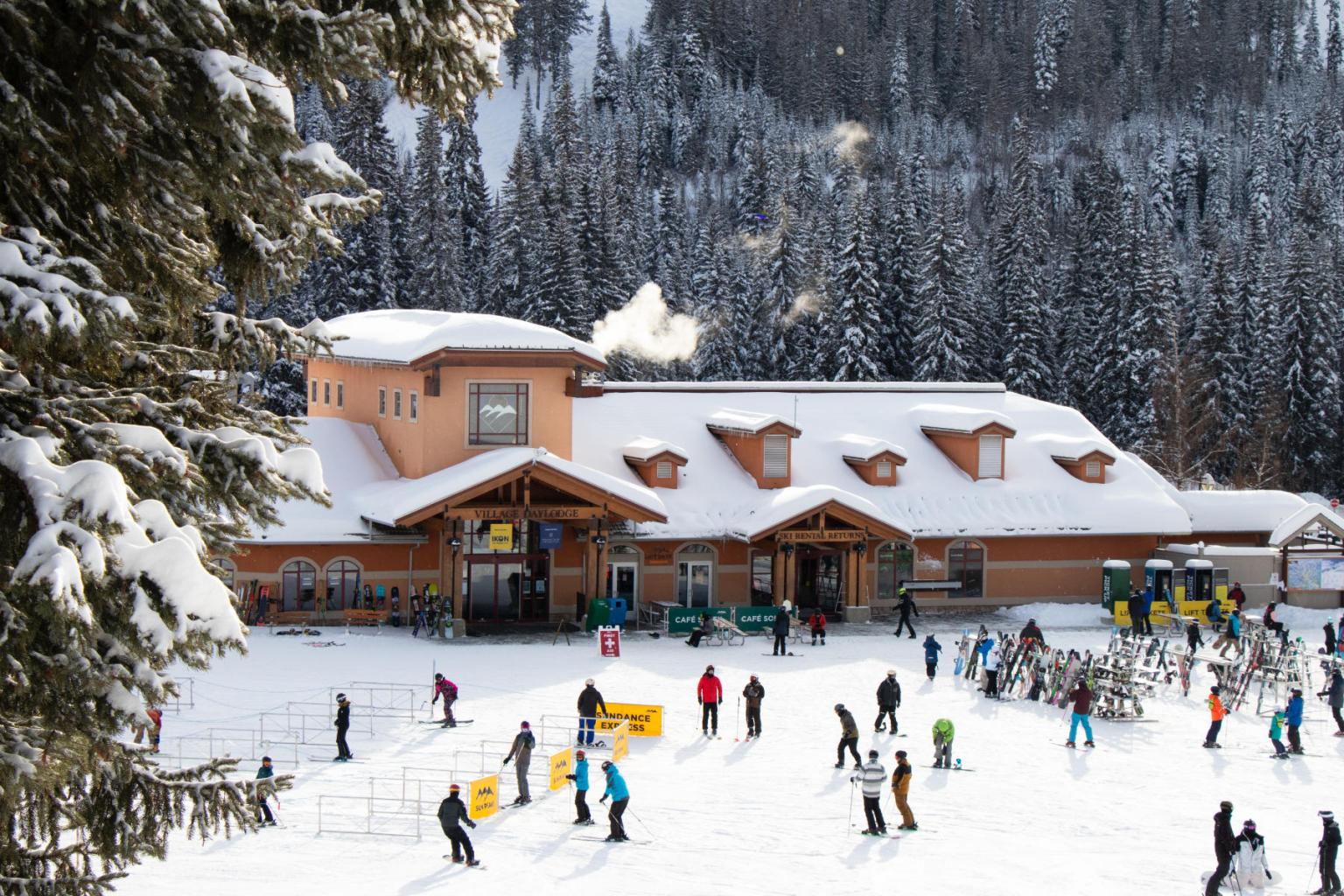 View of a building from slopeside with people skiing in front of it 