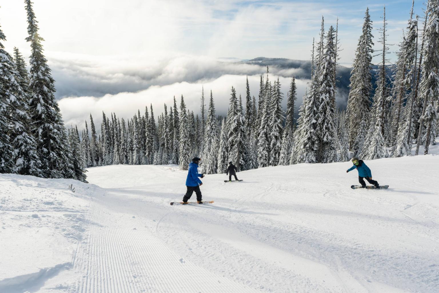 Snowboard instructor with two students riding down a trail with trees and mountain views