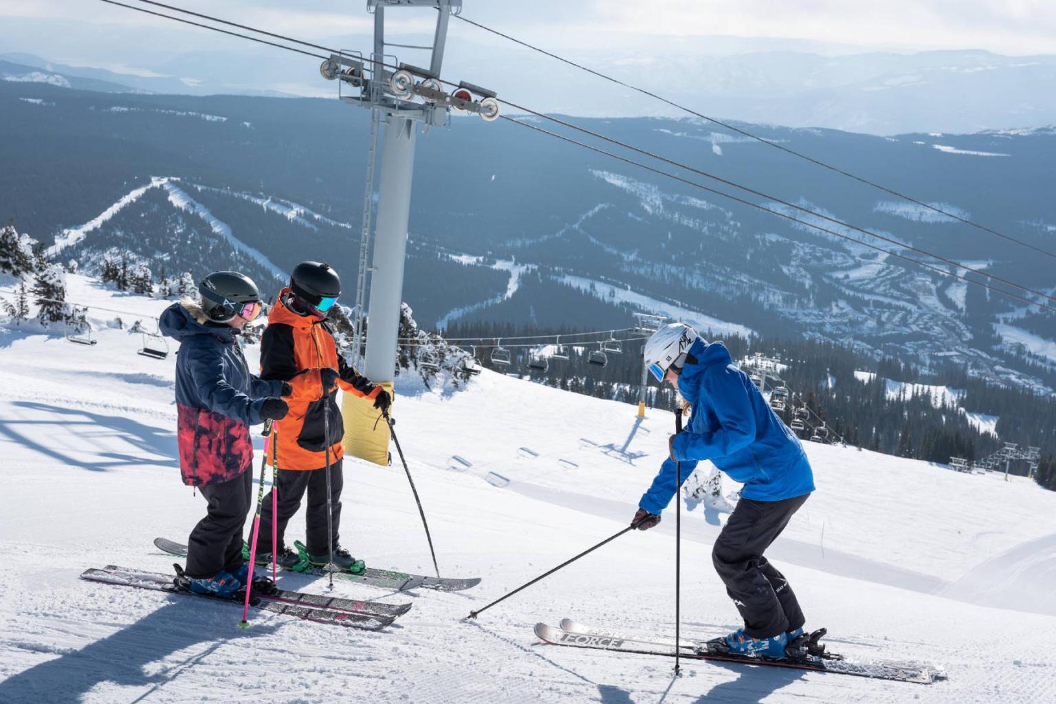Ski instructor with two people on a run with mountain views in the background
