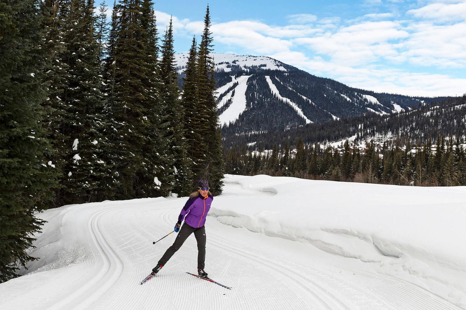 Nordic Skier skiing on a trail with trees and mountains in the background